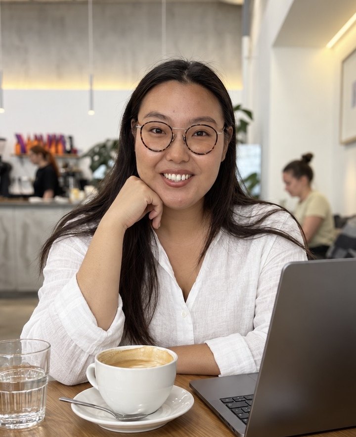 Anna smiling at a café table with a cappuccino and her laptop
